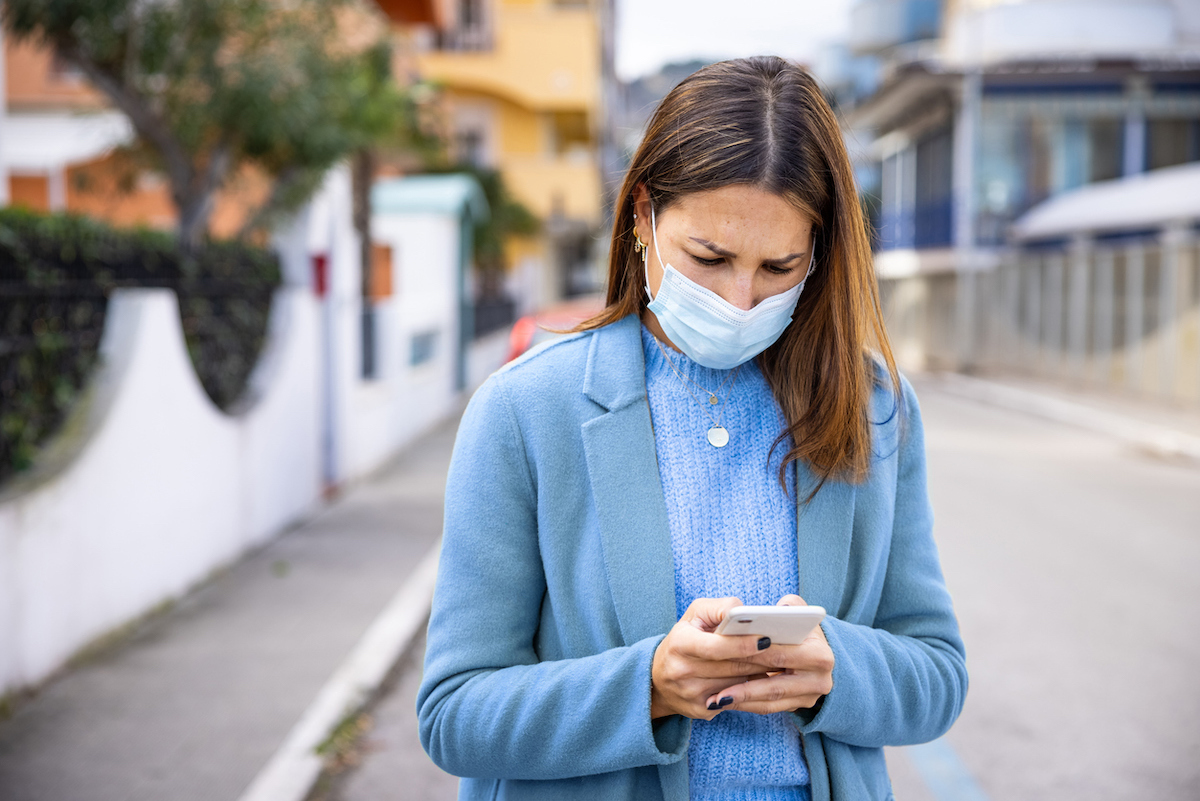 Woman with face protection mask texting on mobile in the street