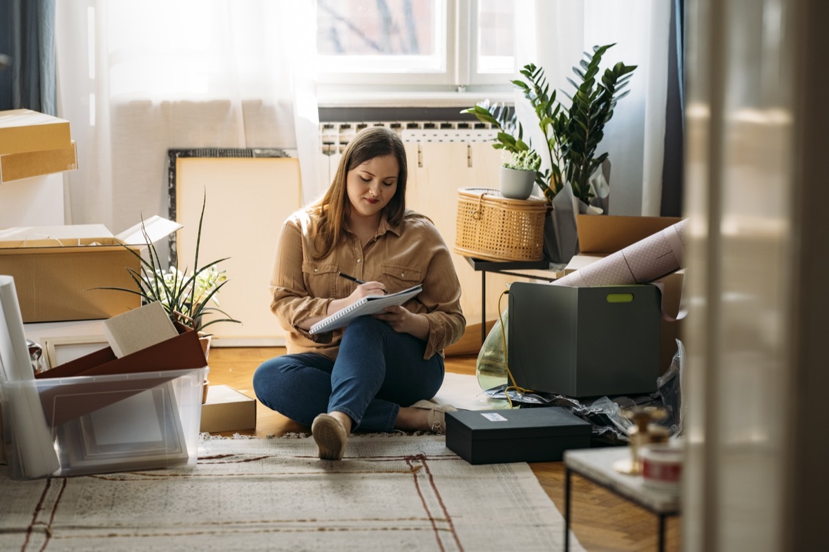 A happy woman moving out, sitting on the floor and making a list of items packed