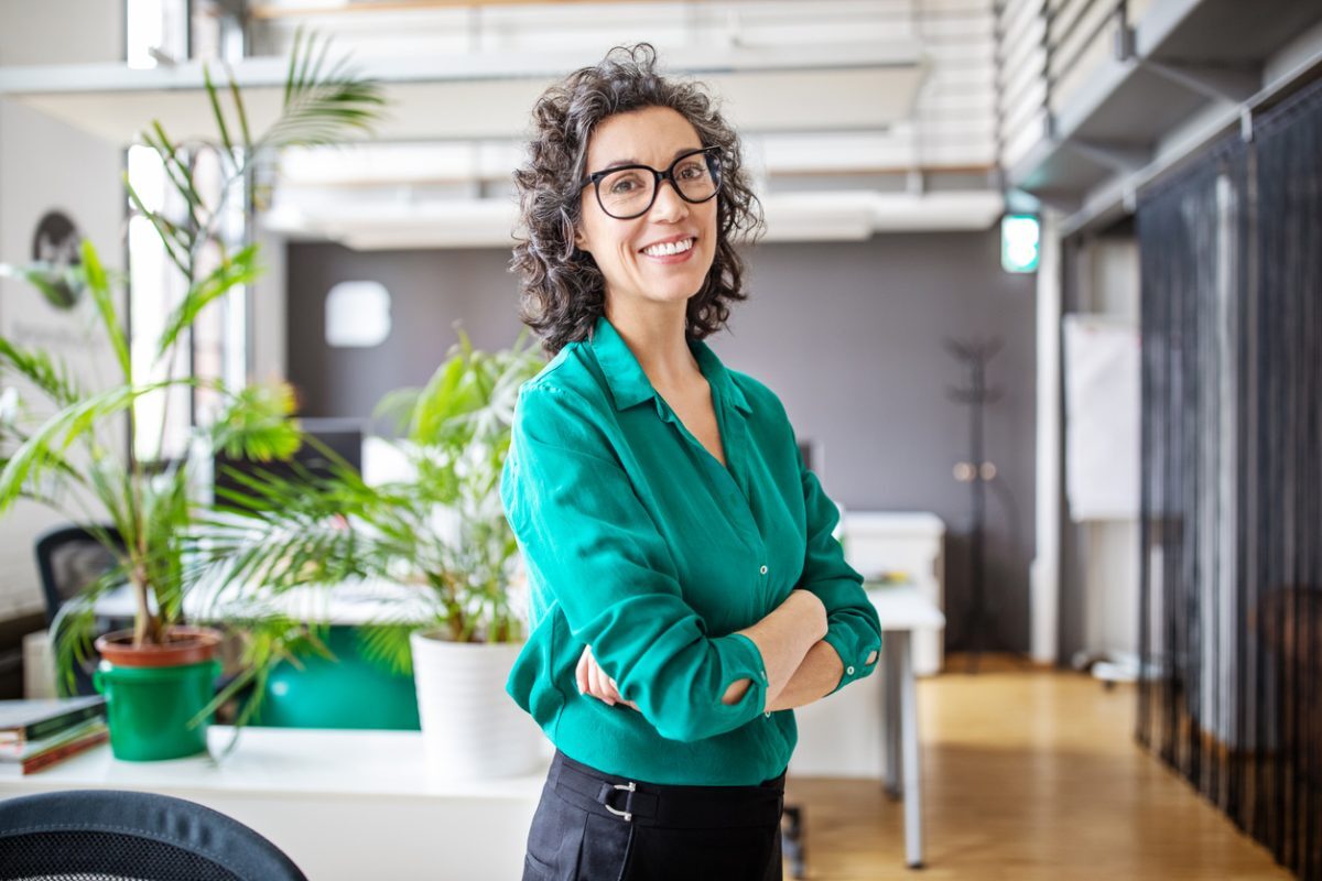 Portrait of happy mature businesswoman standing with her arms crossed. Mid adult female looking at camera and smiling while standing in office.