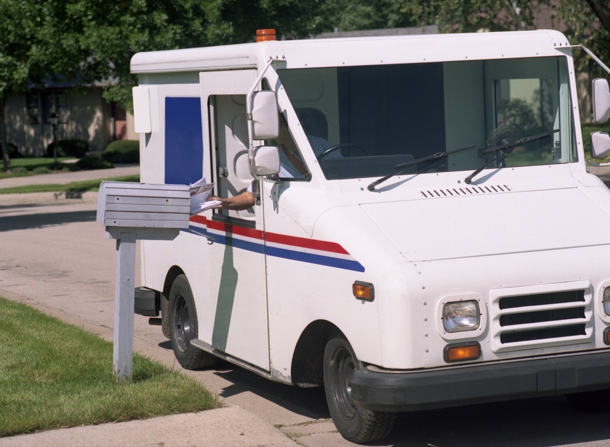 a mail carrier delivers mail, reaches out of the mail truck