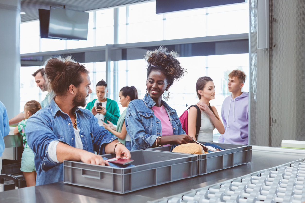 Two travelers placing their items in a bin at an airport security checkpoint