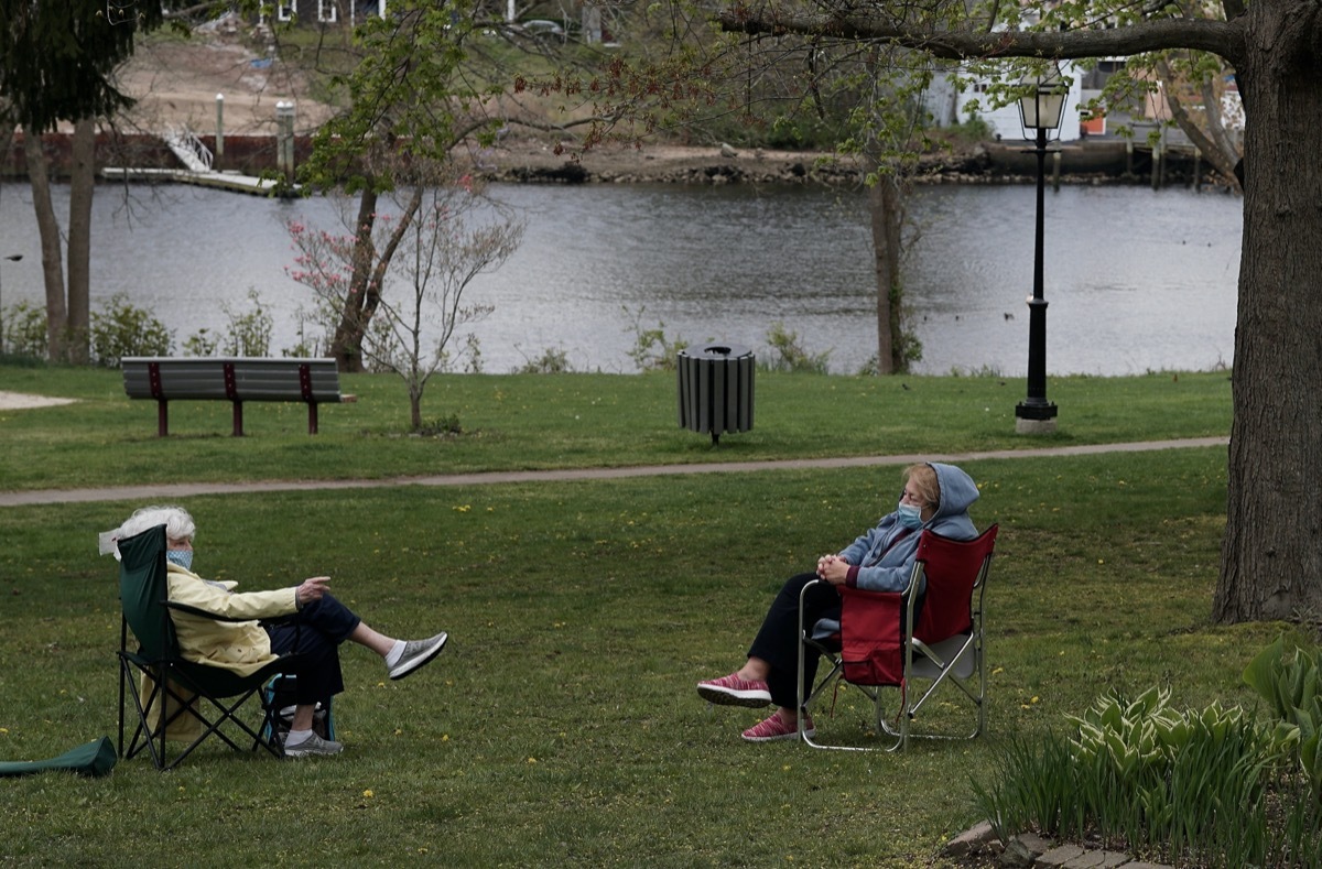 Two masked elderly women maintain social distancing during their conversation in the park