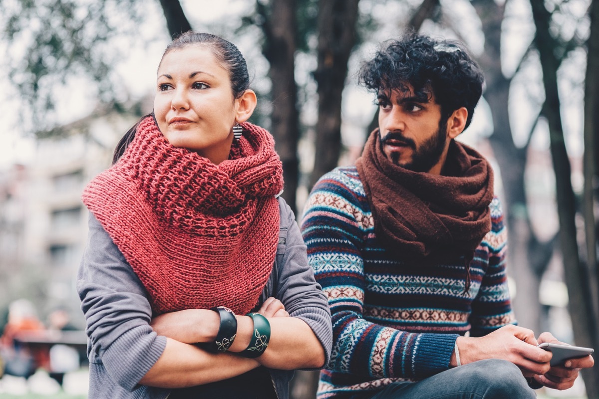 unhappy white woman facing away from middle eastern man on his phone outside in the cold