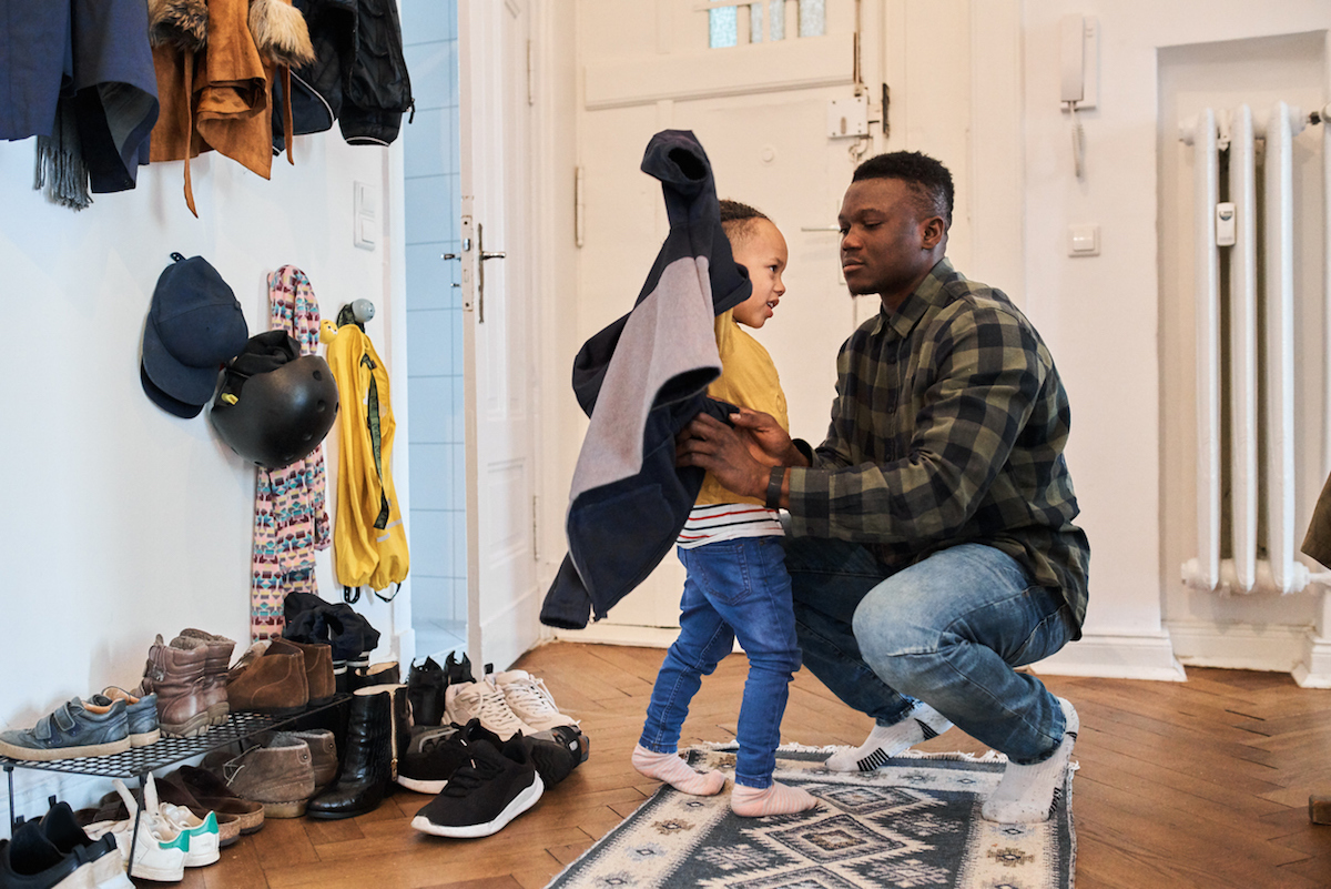 man crouching while helping boy in wearing jacket at home. Father dressing up son before going out of house.