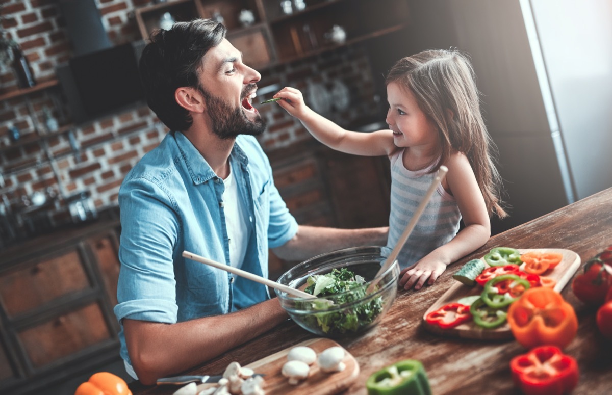 man and his little cute daughter are cooking on kitchen. Making salad