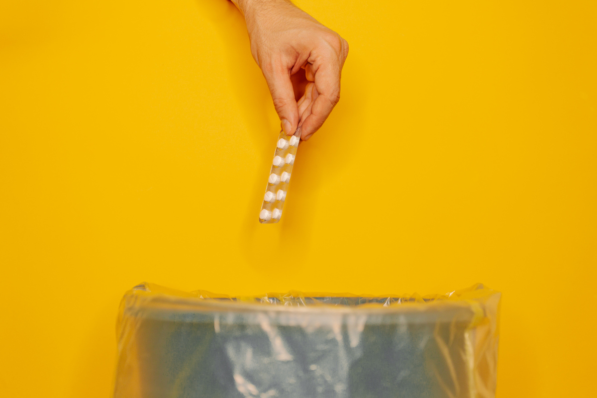 hand throwing pills away on orange background