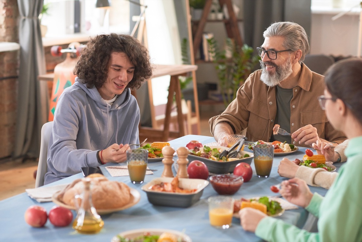 Happy family talking to each other while sitting at the table and having dinner at home