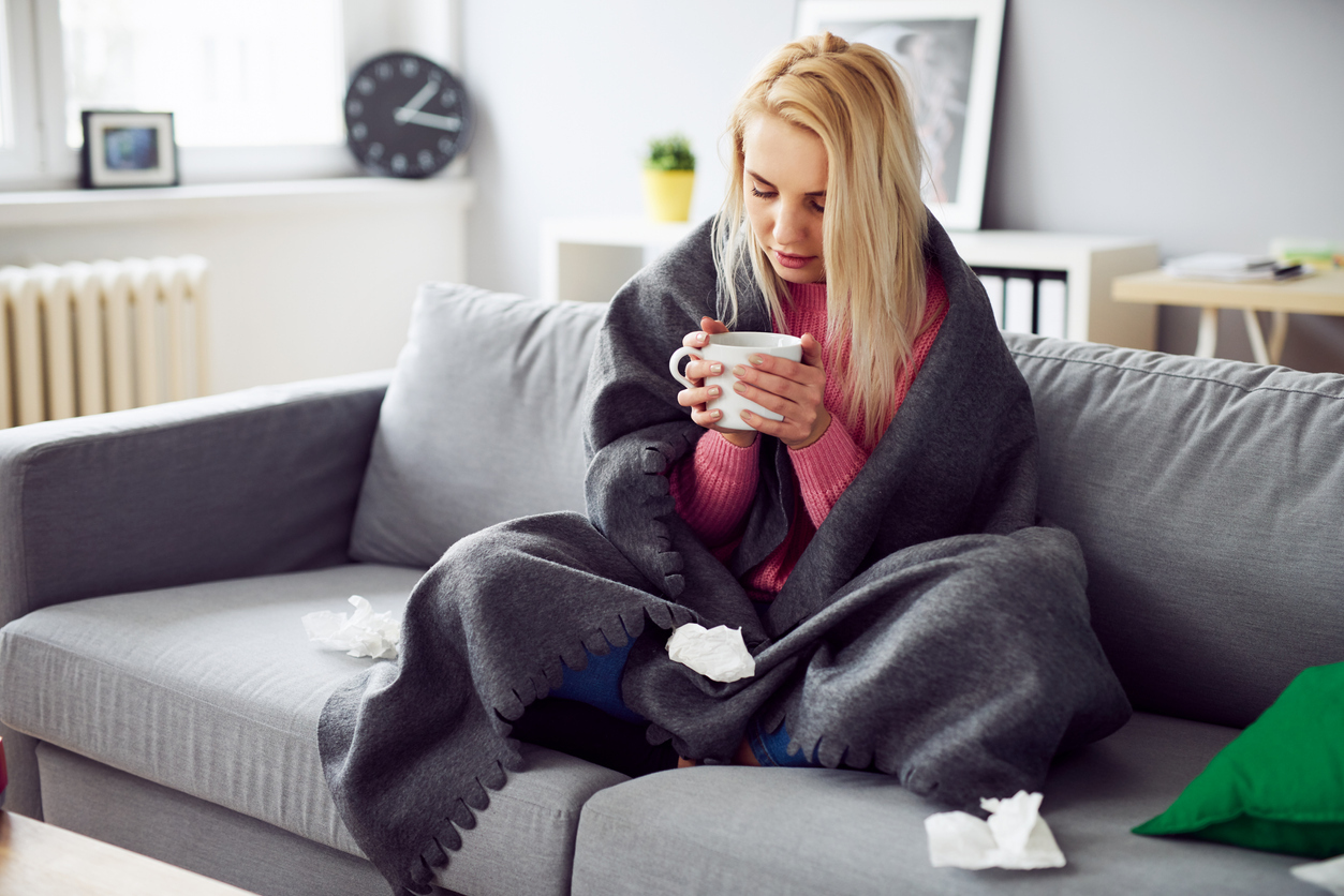 A young woman sitting on the couch with a mug while feeling sick