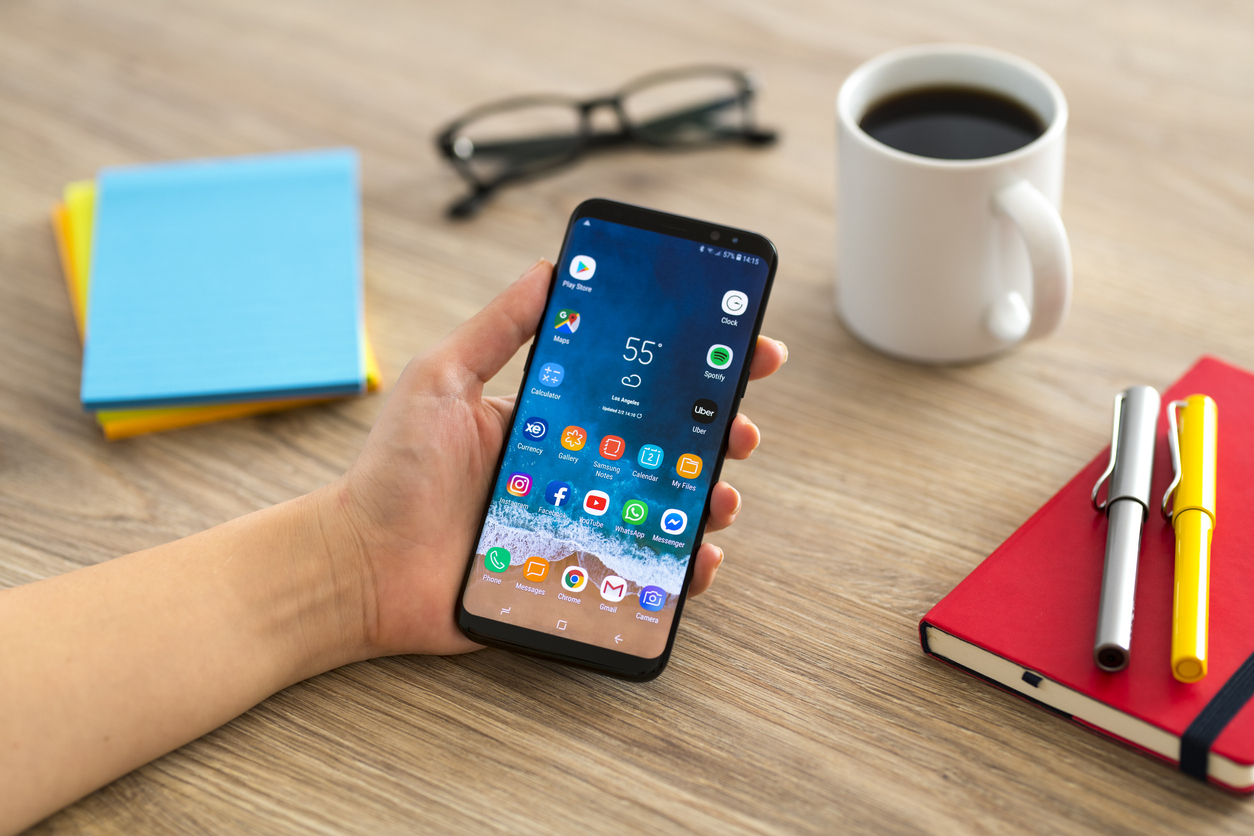 A closeup of a hand holding an Android phone on a desk