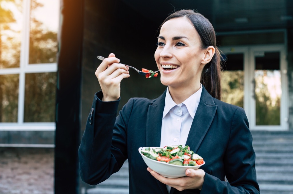 Happy woman eating salad with a fork