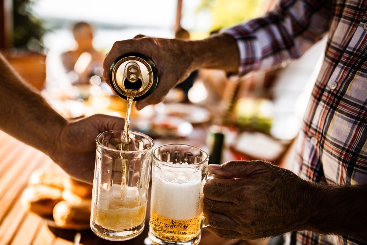 close up of unrecognizable men pouring beer from a can into beer glasses.