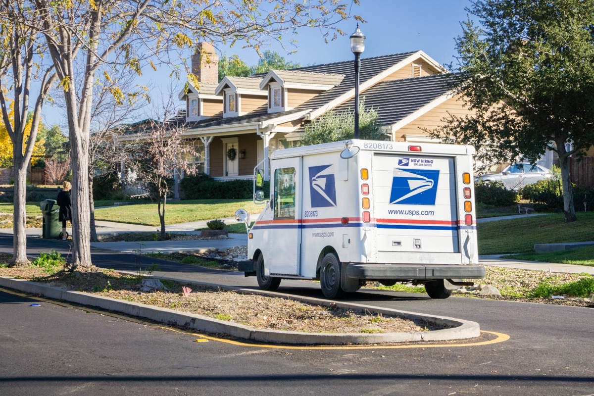 USPS vehicle driving through a residential neighborhood on a sunny day