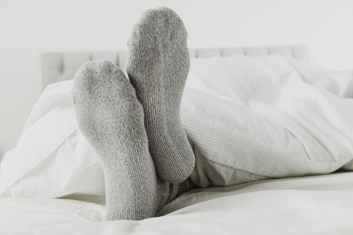 Close up of feet wearing gray socks in bed with white sheet.