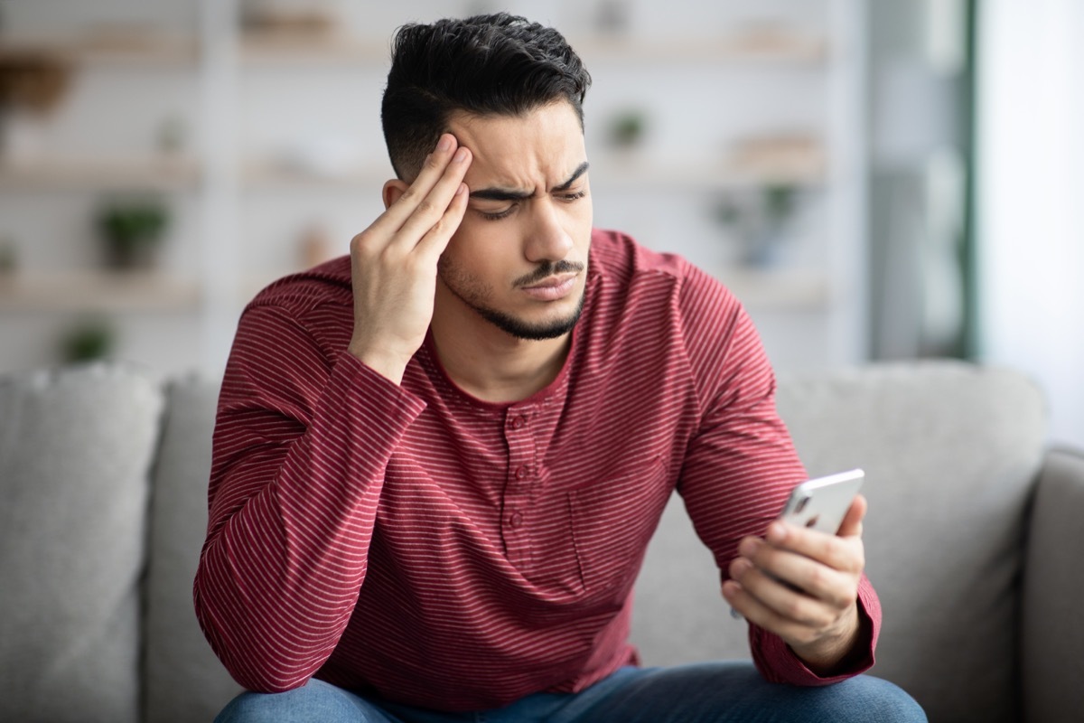 guy sitting on sofa at home, using smartphone,