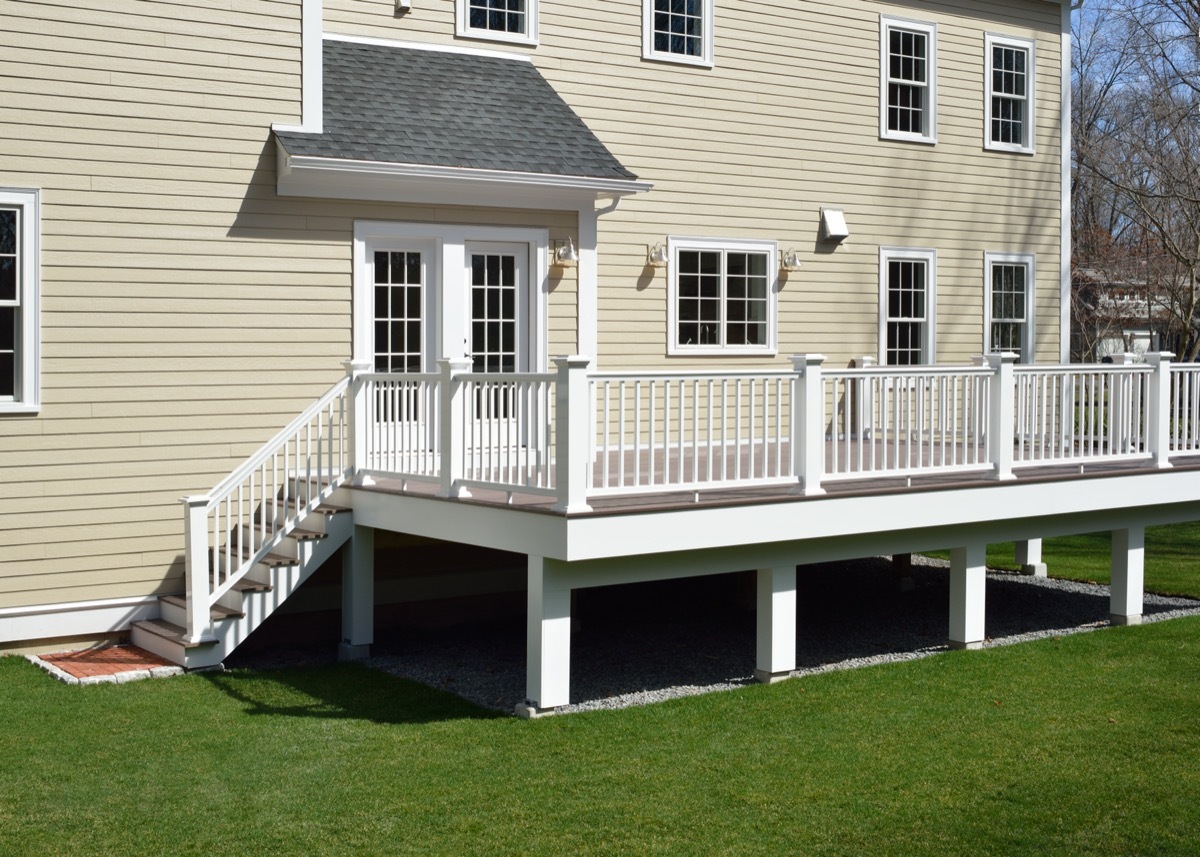 New composite deck. White veranda and railing posts, brown boards, elevated above ground. Showing support frame and gravel under porch.