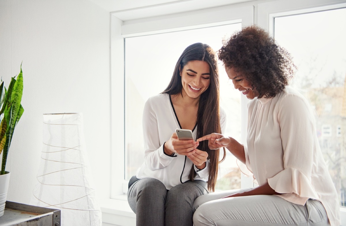 two women looking at phone and laughing, female friendship