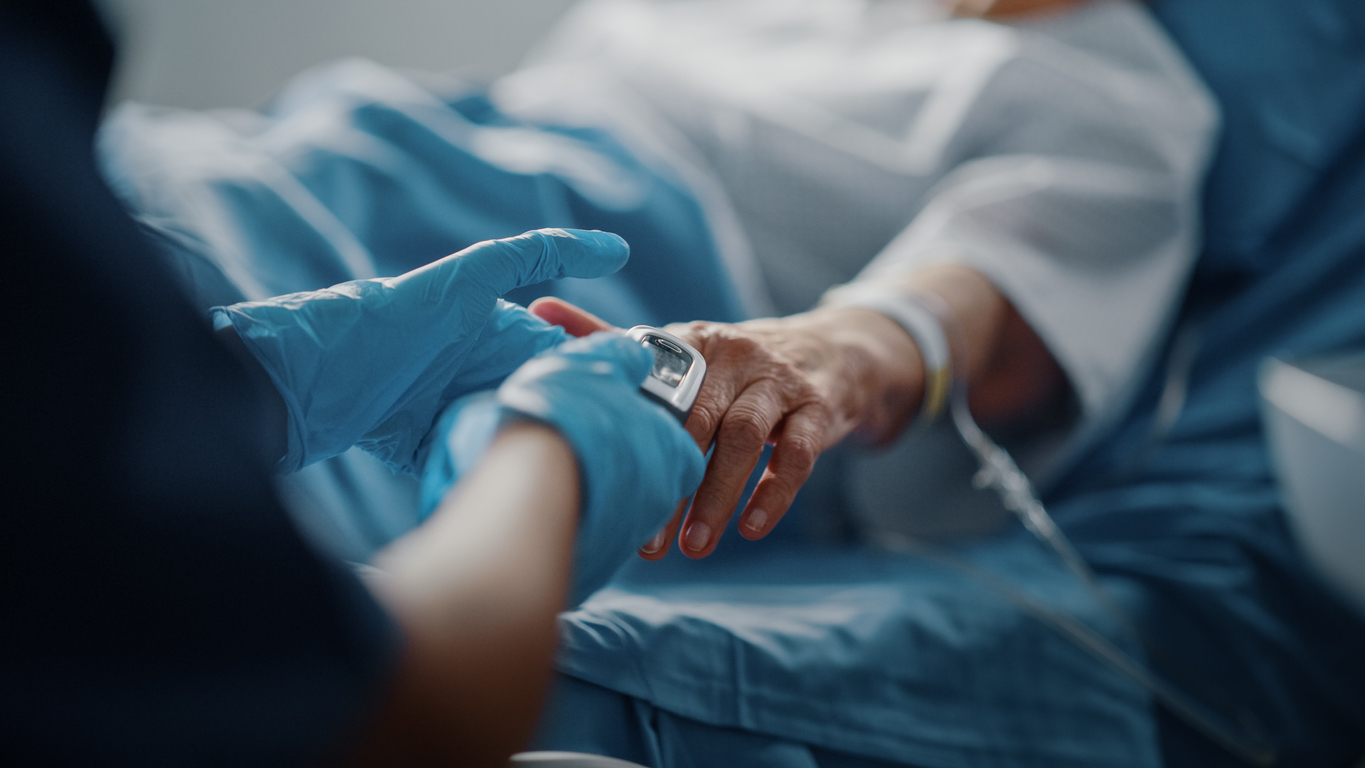 Patient resting on hospital bed having heart rate checked. 