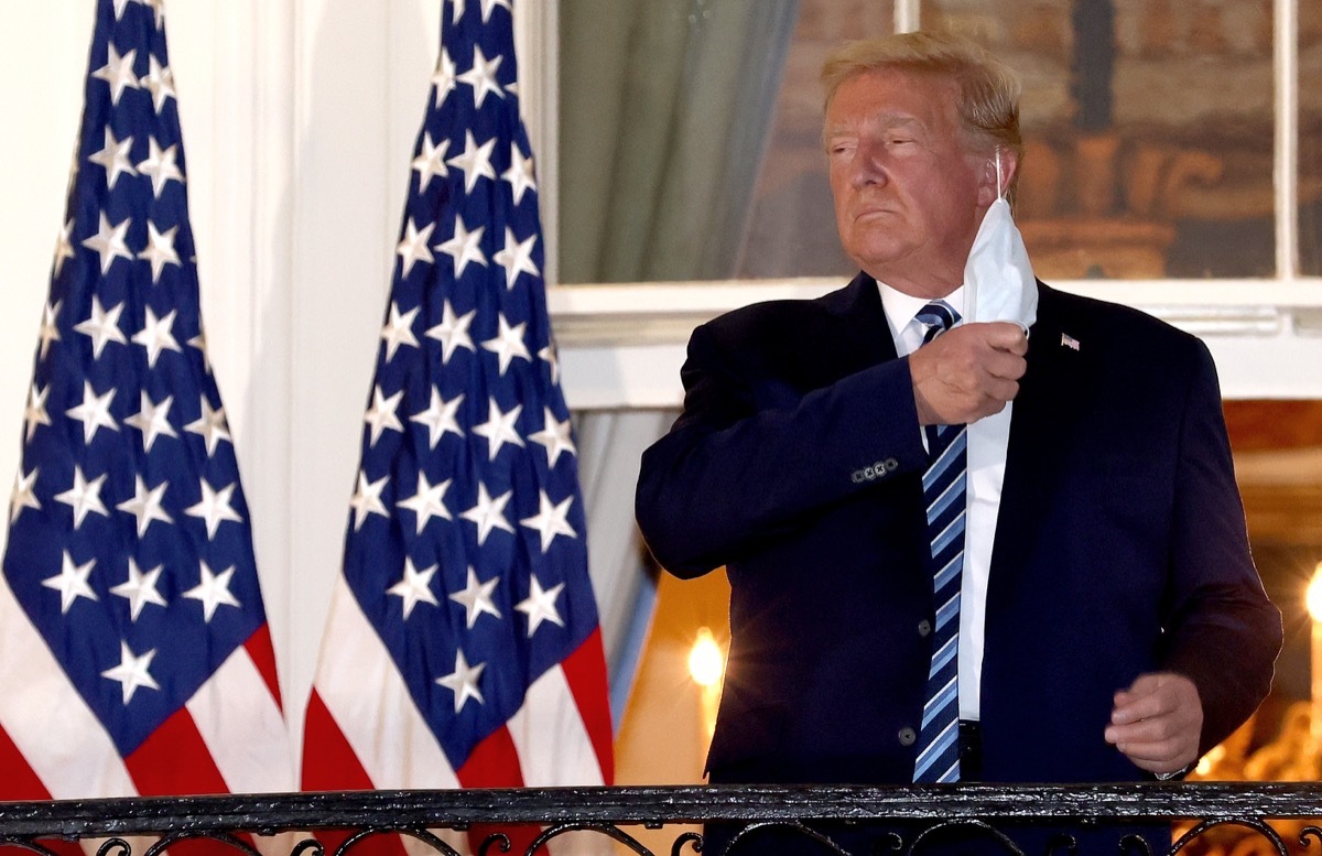 Donald Trump stand by American flags, takes off a white mask, at white house