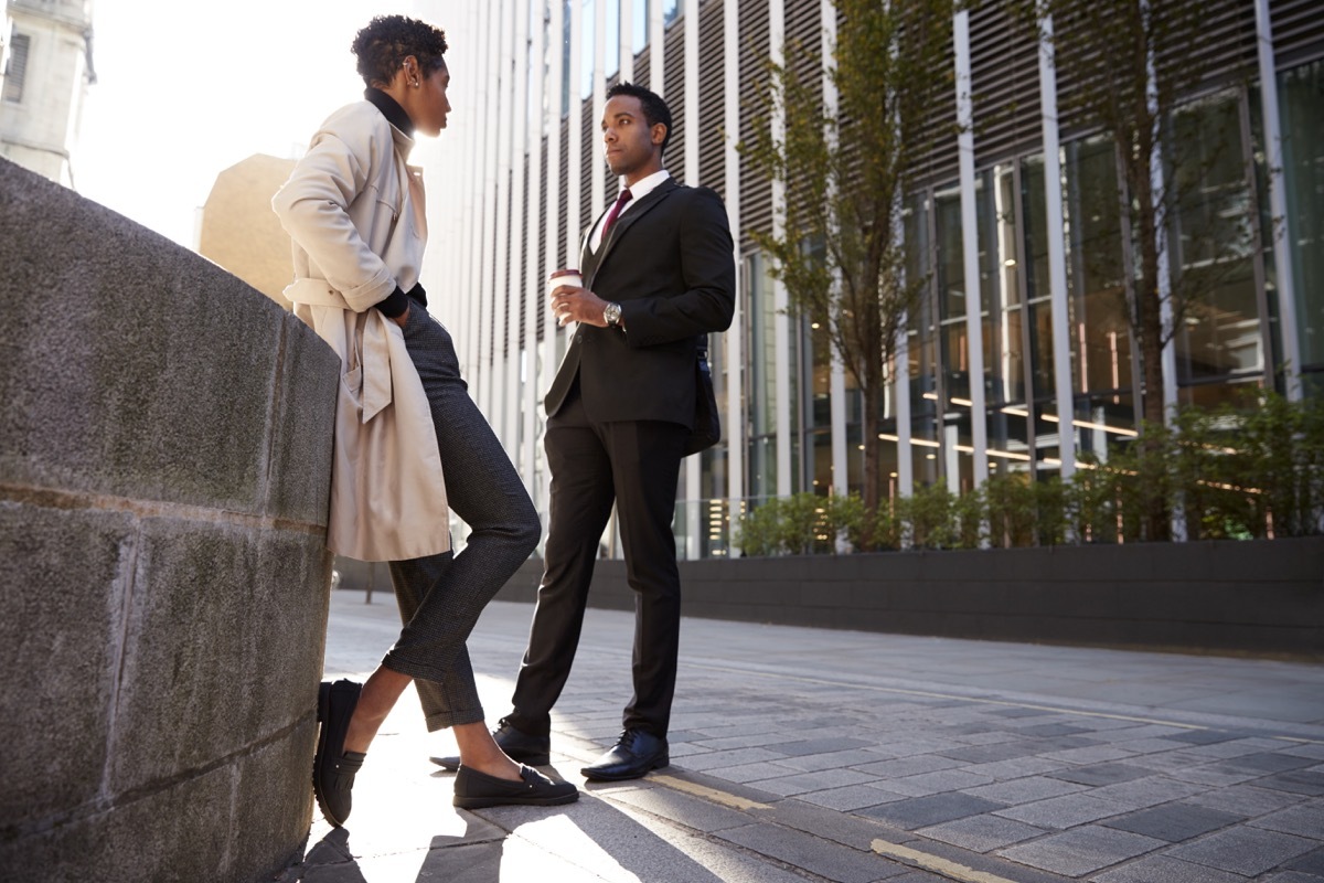 Two young adult colleagues standing on the street talking, low angle