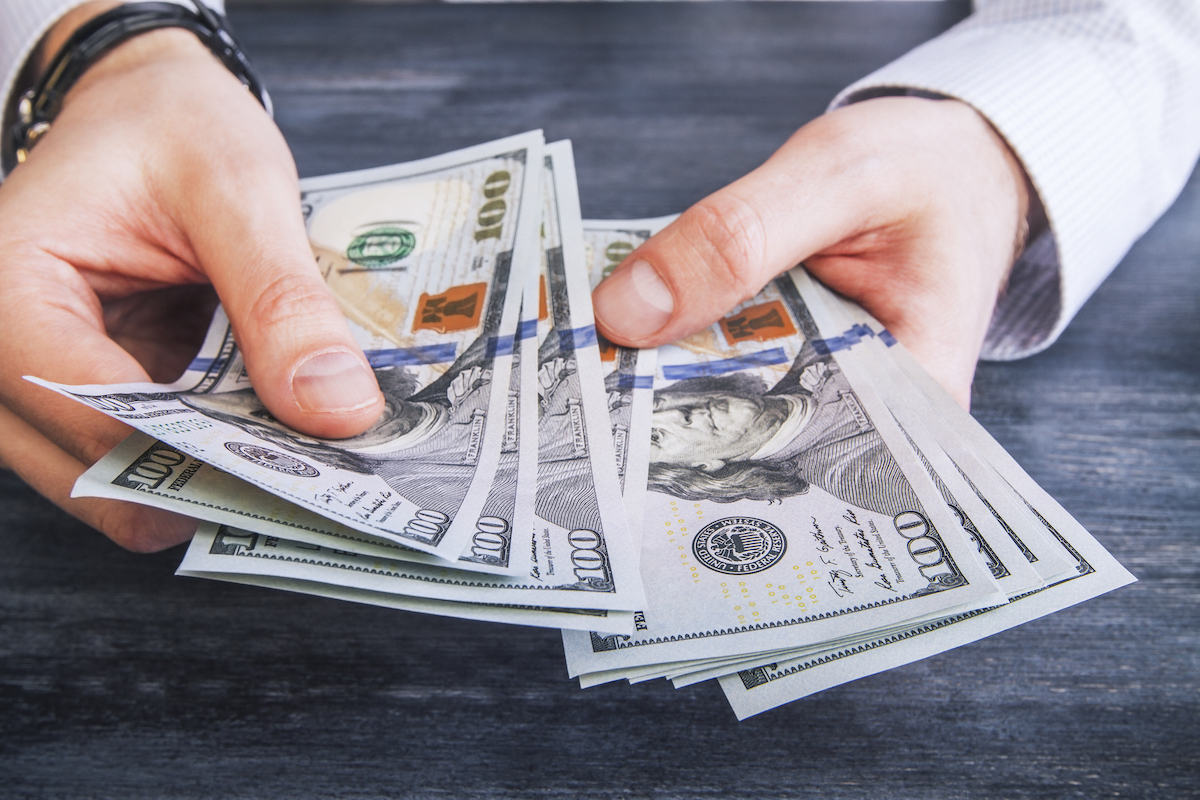 hands counting $100 dollar banknotes on dark wooden surface