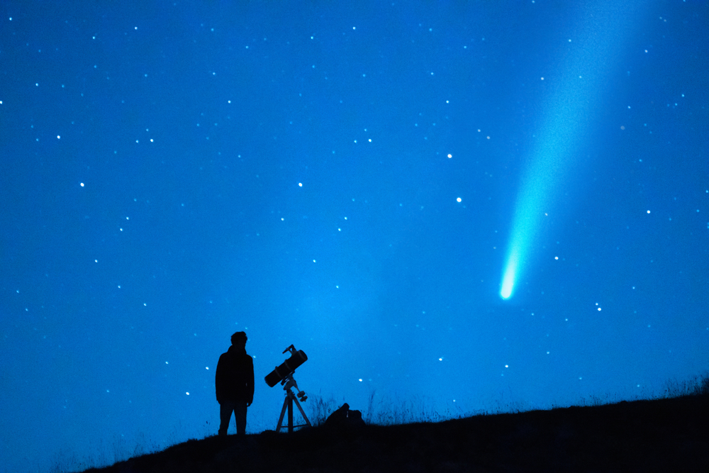 A person stargazing and watching a comet with a long tail in the night sky