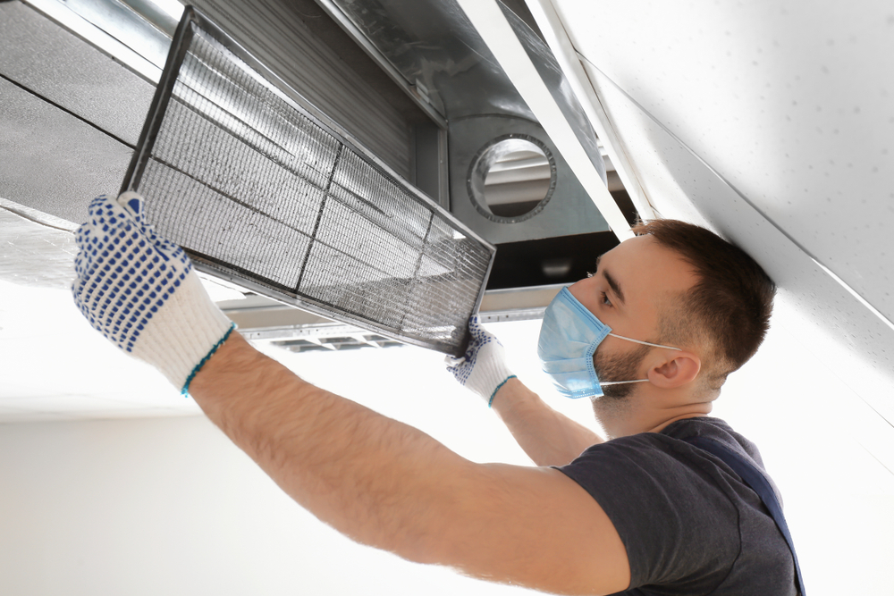 A white male technician cleaning industrial air conditioner indoors