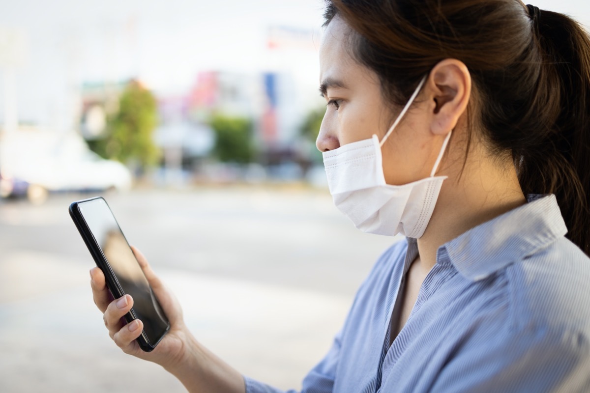 young woman looking at phone wearing mask under nose